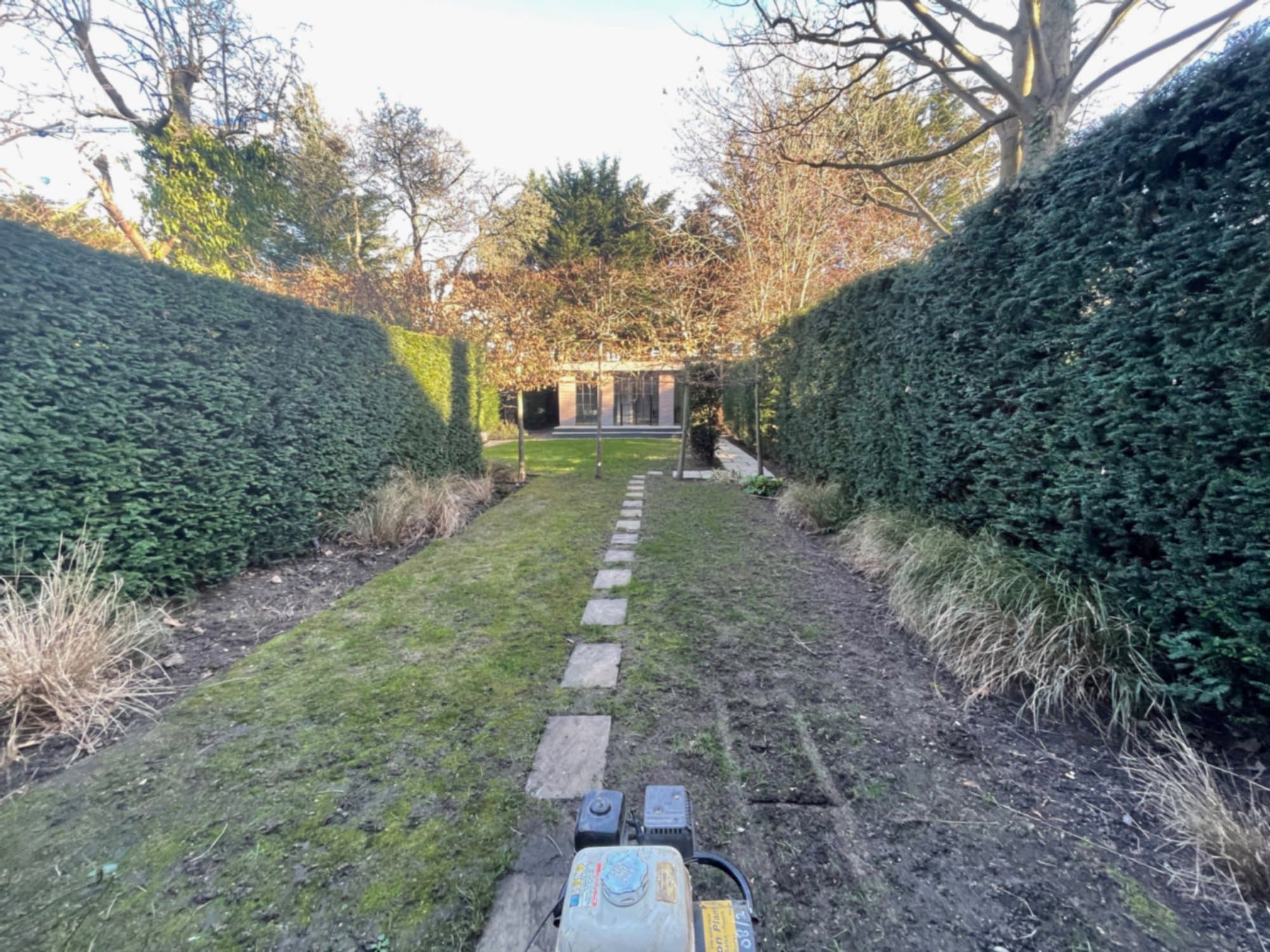 Ground preparation underway, mid-restoration, framed by the established yew hedging