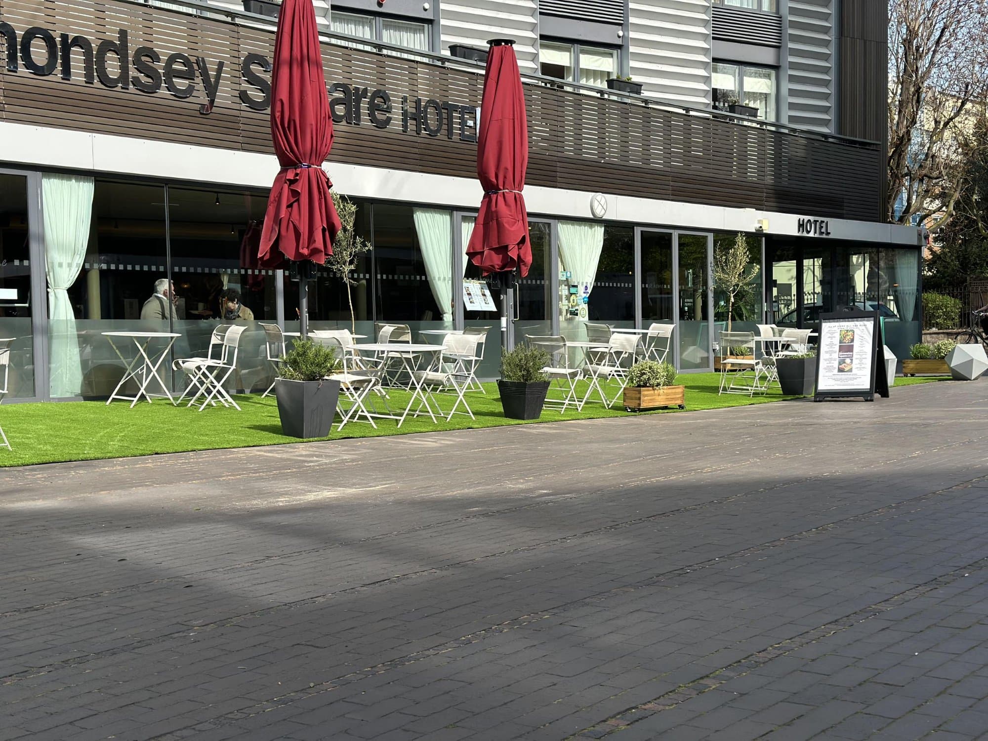 Angled view looking down the length of the finished street-level lawn with café tables lining the hotel