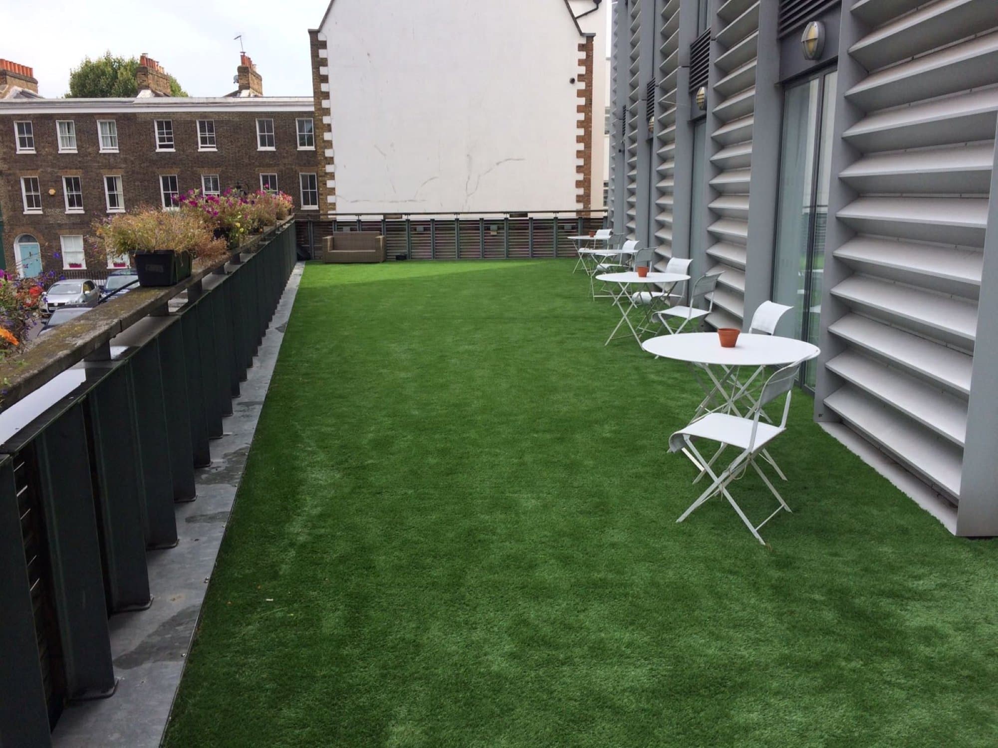 Wide view of the private first-floor terrace after install, with café tables set out along the freshly laid lawn and Georgian terraces across the square in the background
