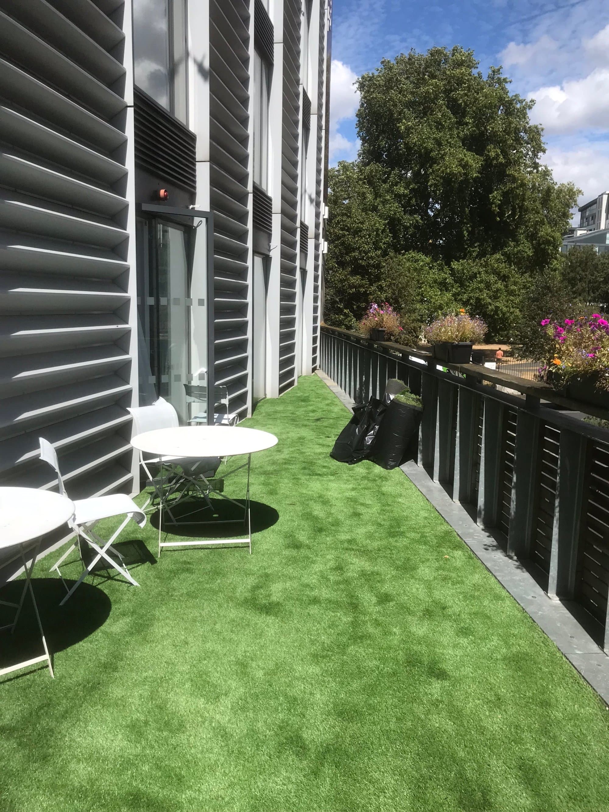 A narrower stretch of the first-floor terrace with artificial lawn wrapping past architectural cladding and planters