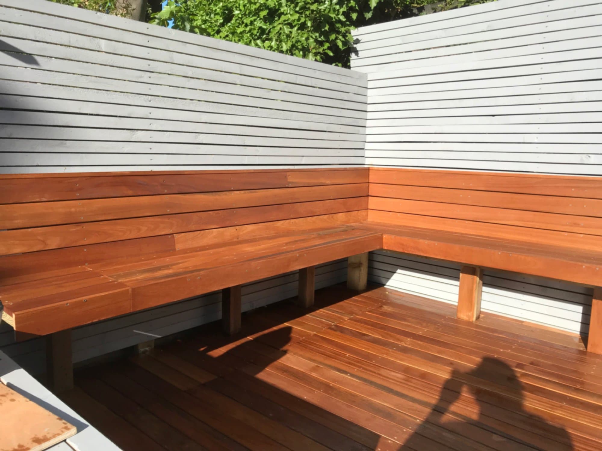 Built-in hardwood corner bench against pale grey slatted fencing