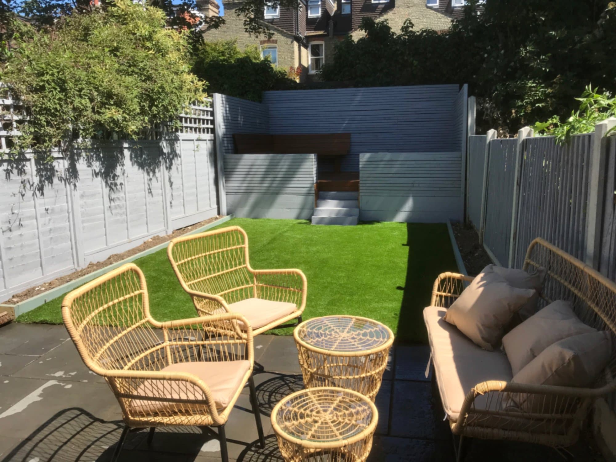 Finished Bounds Green rear garden with hardwood decking, artificial lawn, rattan seating and pale grey slatted fencing