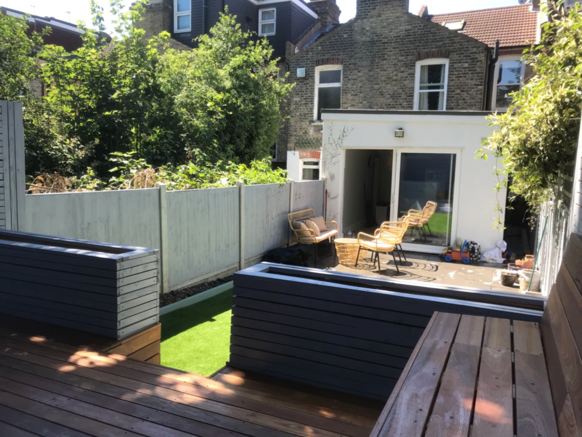 Hardwood decking, dark planters and lawn seen from the far end of the garden