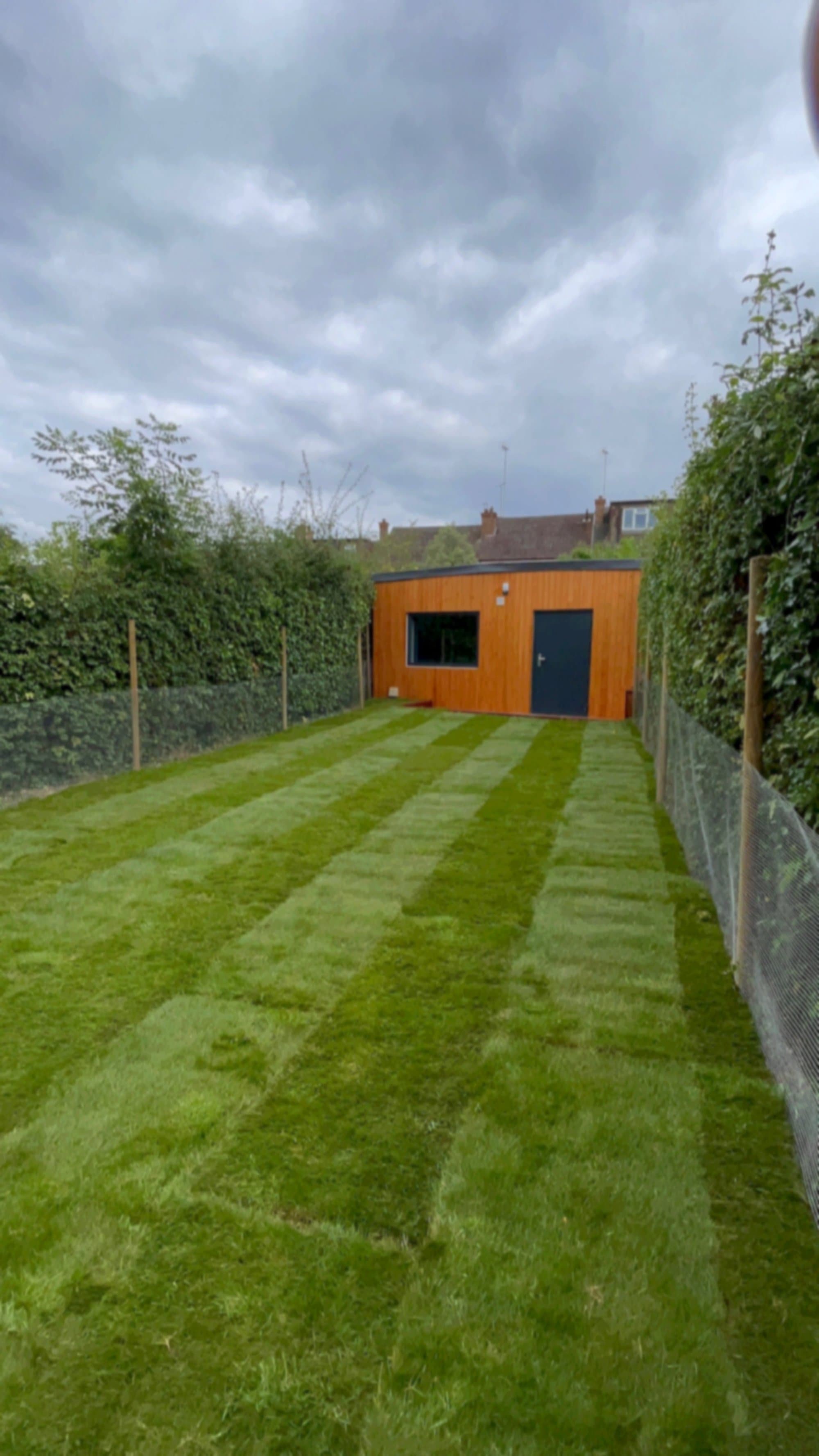 A long Muswell Hill back garden with freshly laid striped turf running down to a cedar garden studio at the far end
