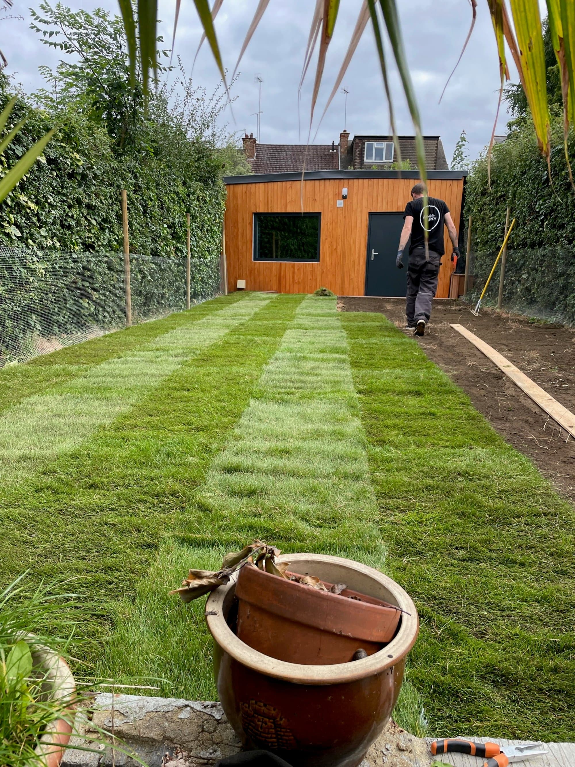 A Pullinger Landscapes team member walking down the freshly laid lawn towards the client's garden studio